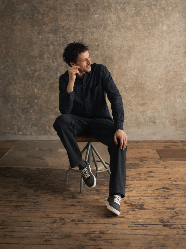 Man sitting wearing european Italian black leather and suede sneakers with white laces and white rubber soles