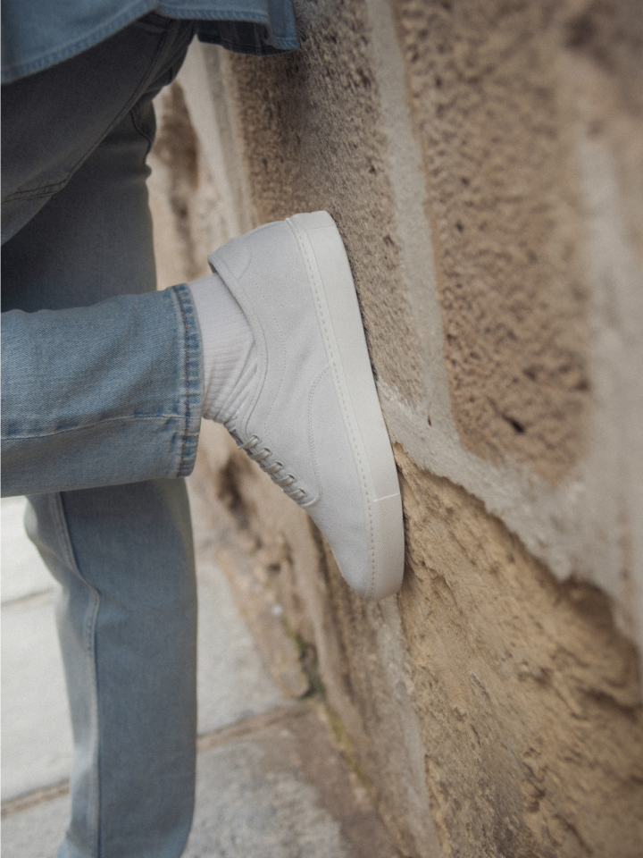 Close-up of men's Italian white suede sneaker with laces and white rubber soles leaning on a wall