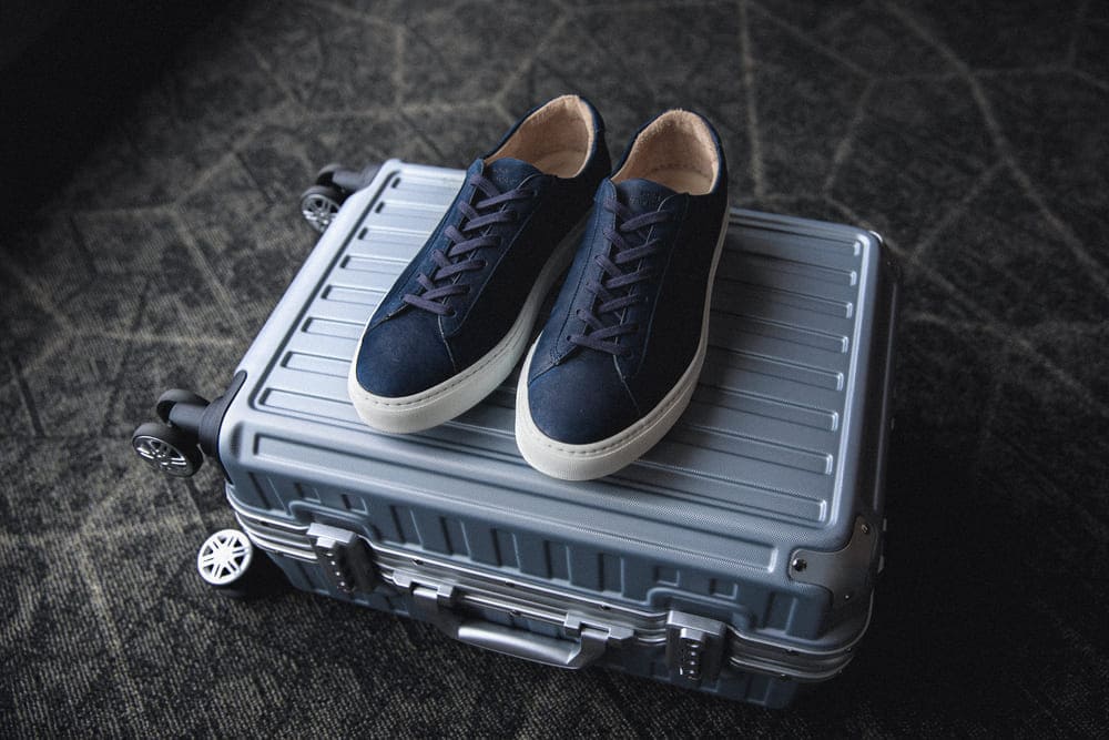 Navy Capri low-top sneakers resting on a hard-shell suitcase for compact travel packing