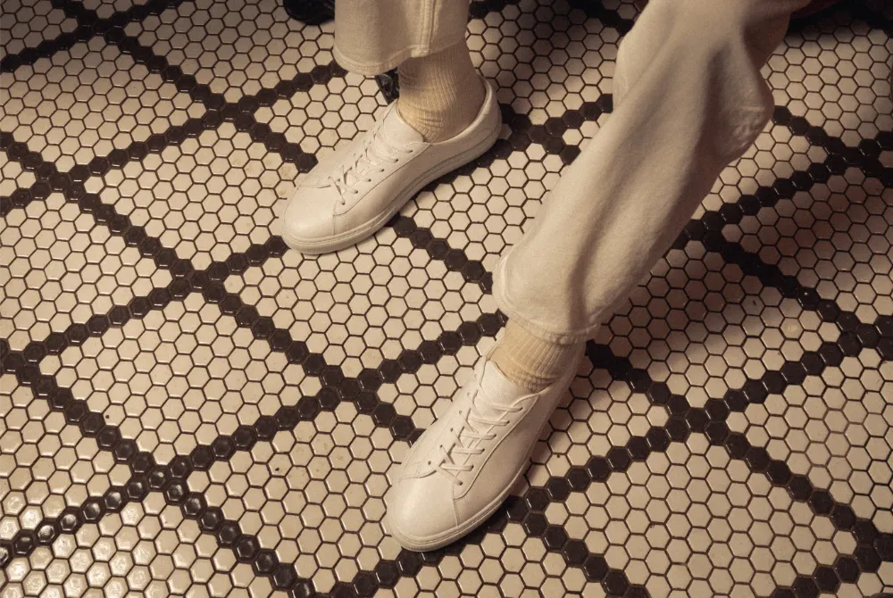 Person wearing white low-top sneakers with cream trousers on a patterned tile floor