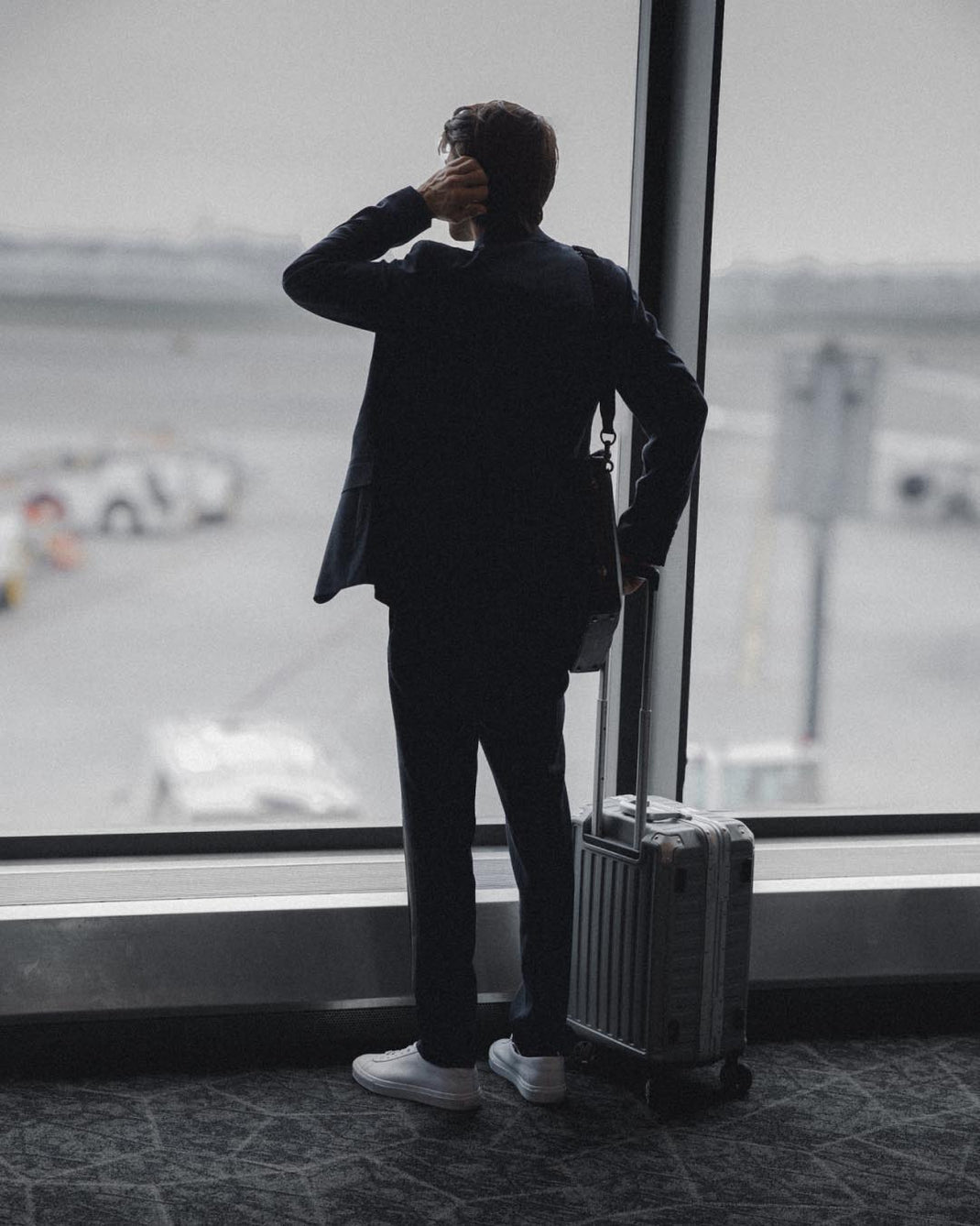 Man wearing white low-top sneakers and standing with a suitcase in an airport