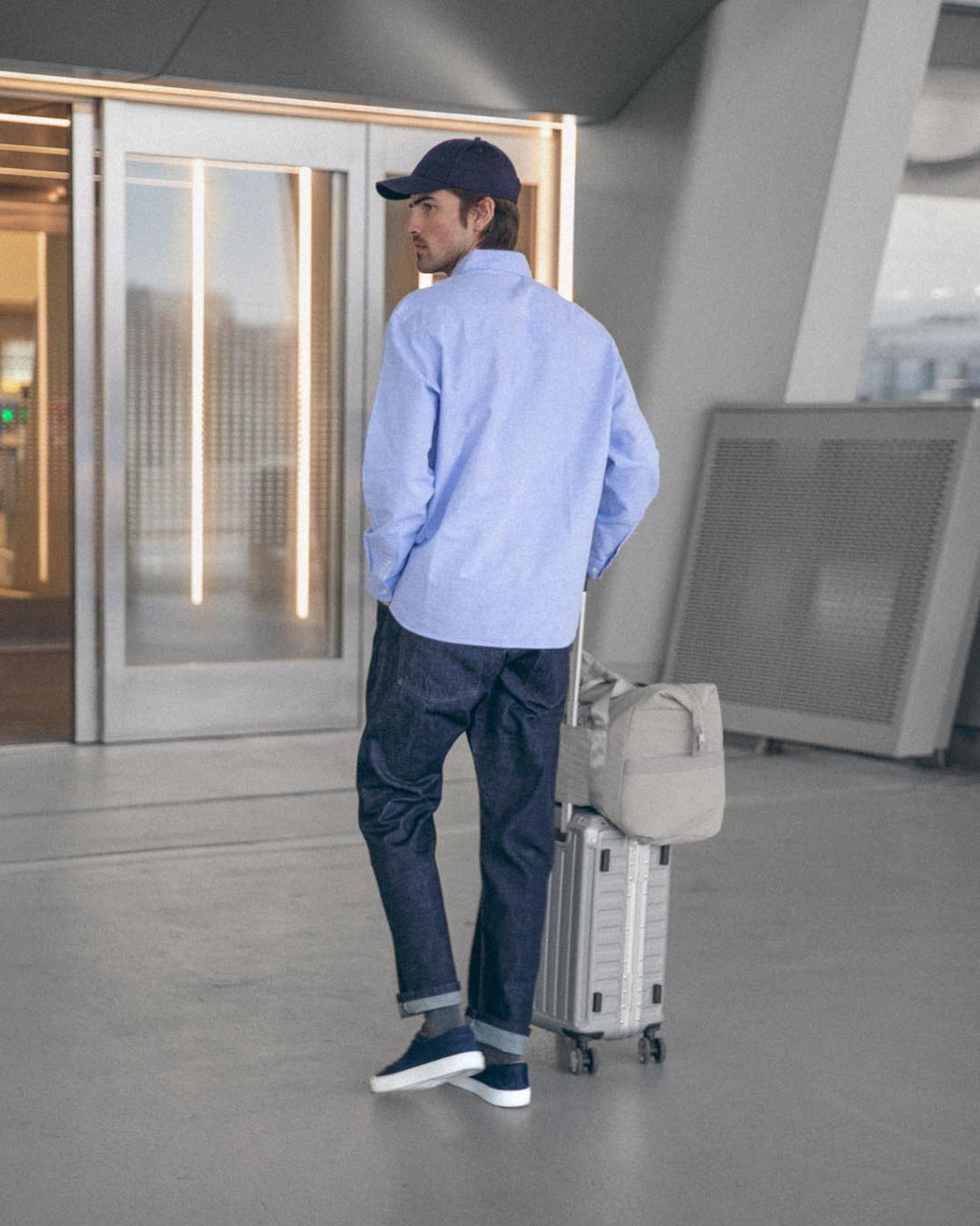 Man wearing blue Capri nubuck low-top sneakers while pulling a suitcase through an airport terminal