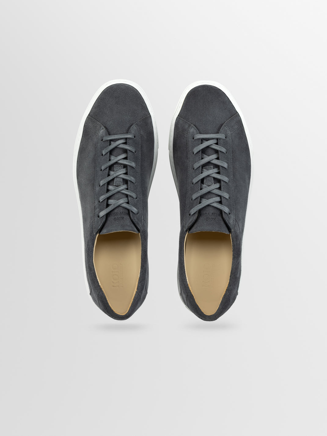 Top view of men’s grey suede low-top sneakers showcasing lace-up fronts and white rubber soles on a light gray background