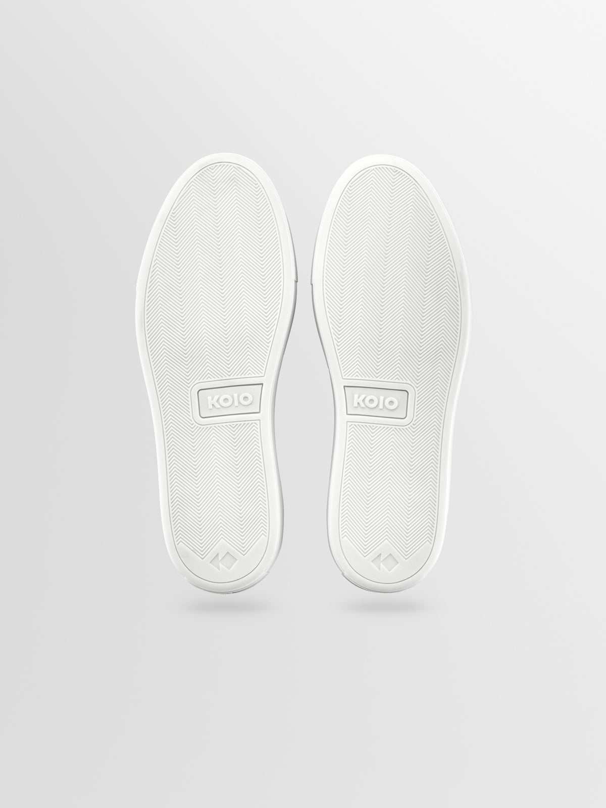 A pair of white low-top sneakers shown from the sole view, featuring a textured rubber outsole.