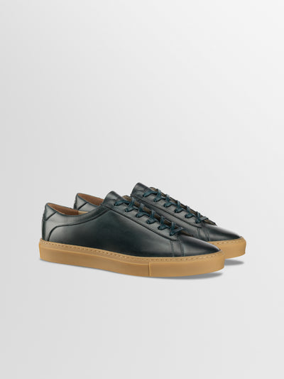 Three-quarter view of Capri in Antica Forest men’s dark green leather low-top sneakers with gum rubber soles on a light gray background
