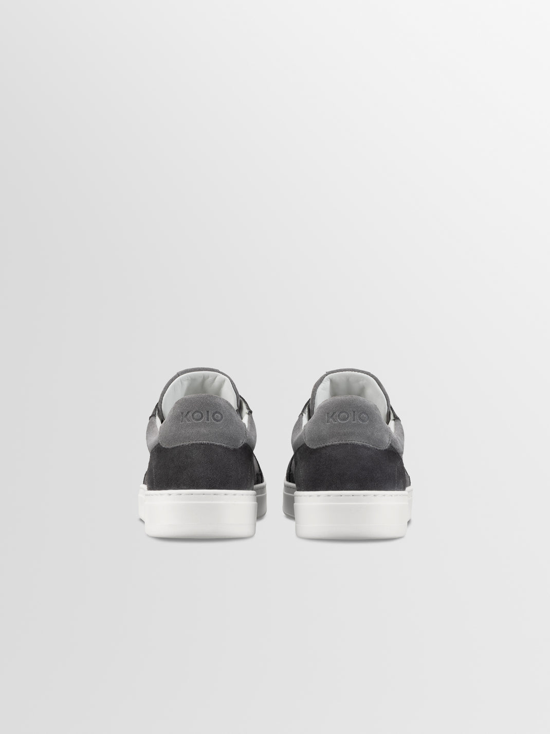 Rear view of Carrara ash gray suede low-top sneakers showcasing KOIO heel branding and white rubber soles against a light gray background