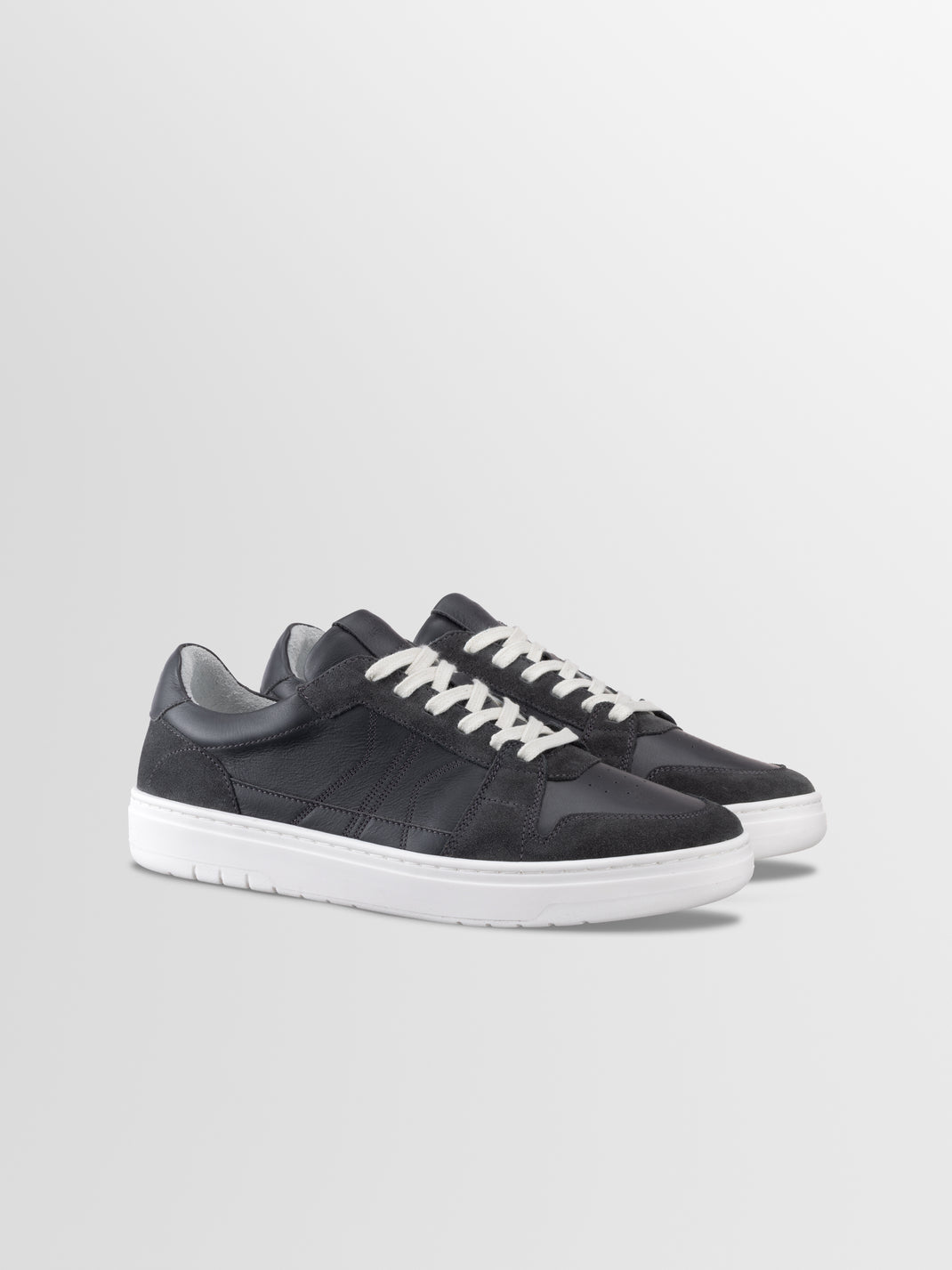 Three-quarter view of Carrara men’s black suede low-top sneakers showcasing white laces and soles on a light gray background