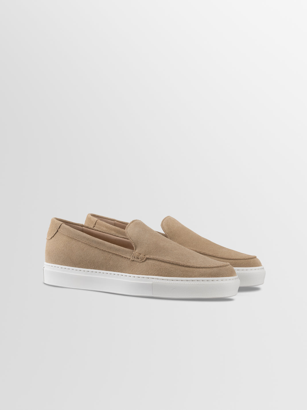 Three quarter view of Lido in Fawn men’s beige suede slip on loafers showcasing white rubber soles against a light gray background