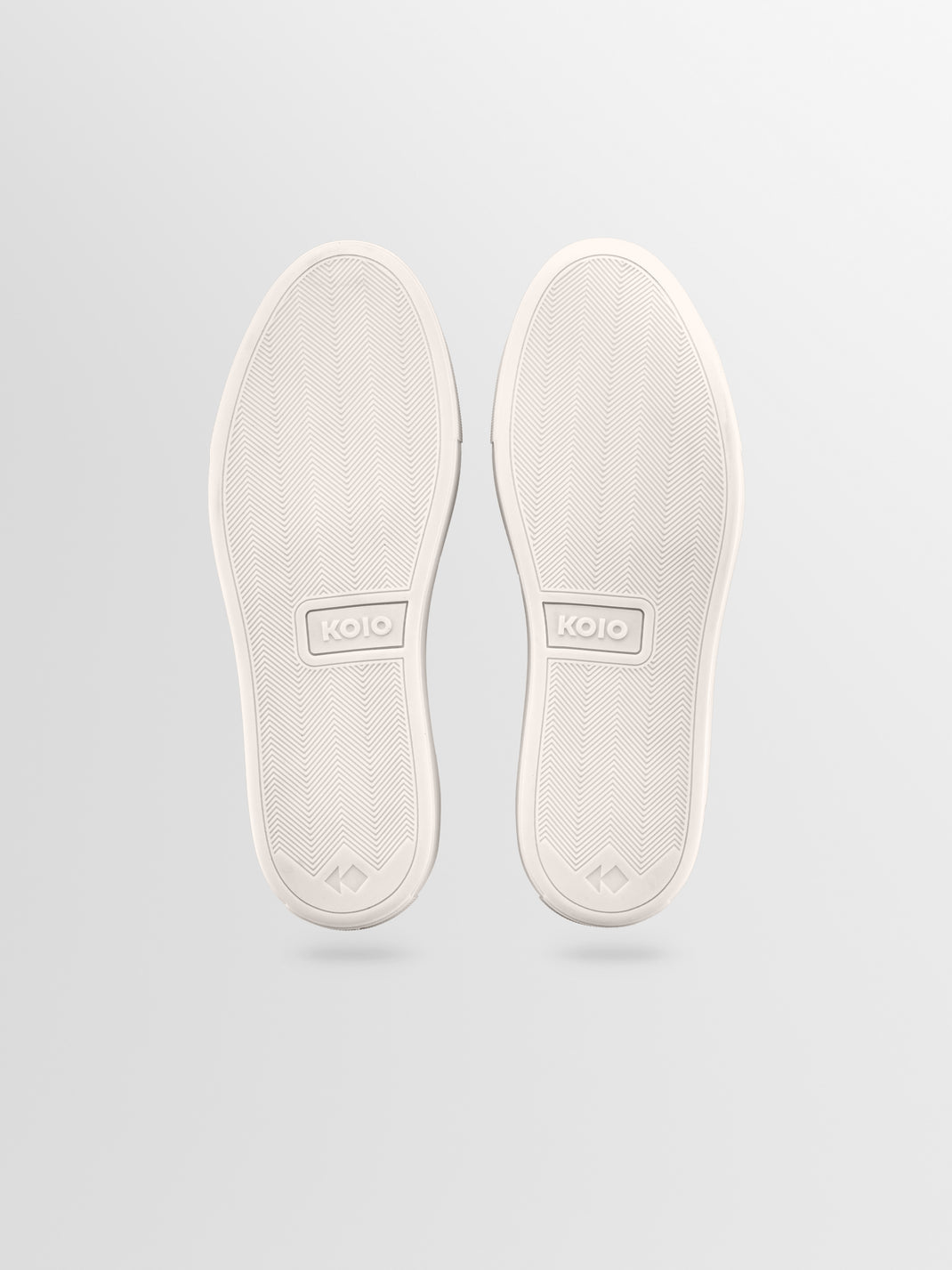 Bottom view of Lido suede slip-on loafers in Mineral showcasing textured KOIO soles against a light gray background