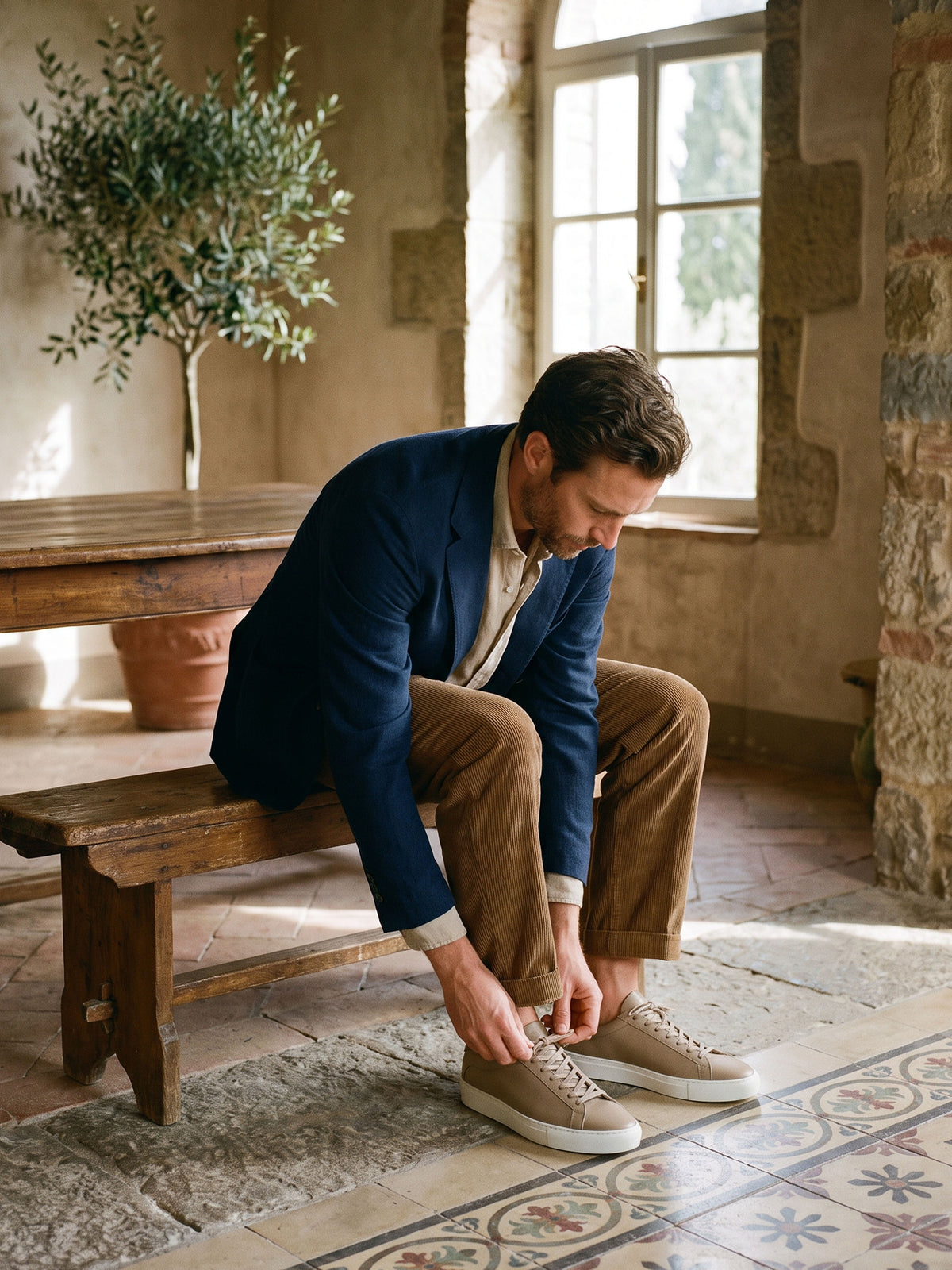 Man sitting on a bench in a room wearing a navy jacket, khakis and men