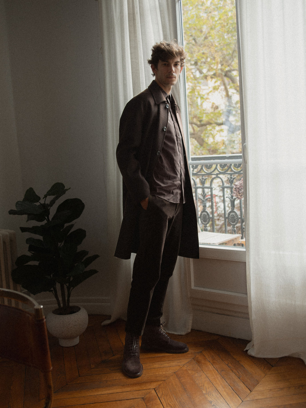Man wearing brown suede lace-up Bergamo boots beside a window in a warmly lit room