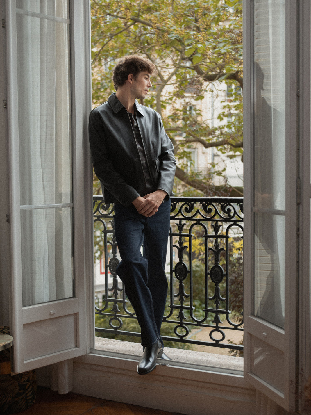 Man wearing black leather Chelsea boots while standing in an open balcony doorway