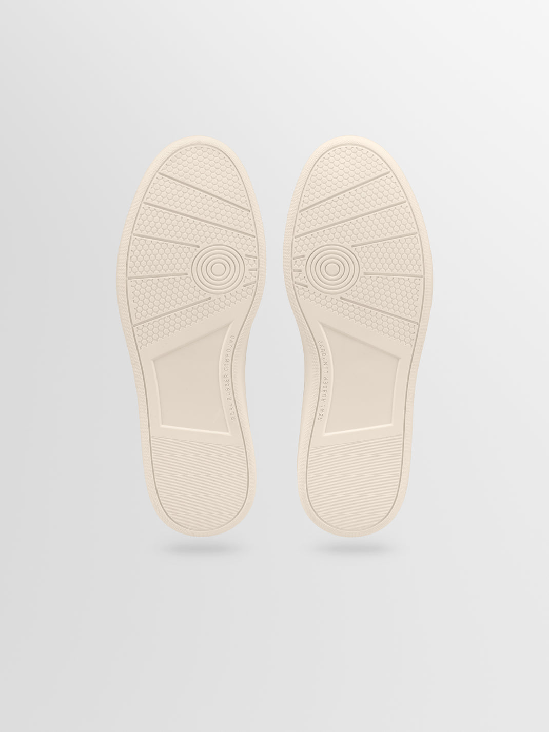Bottom view of the Monza in Latte low-top sneakers showcasing textured rubber soles on a light gray background
