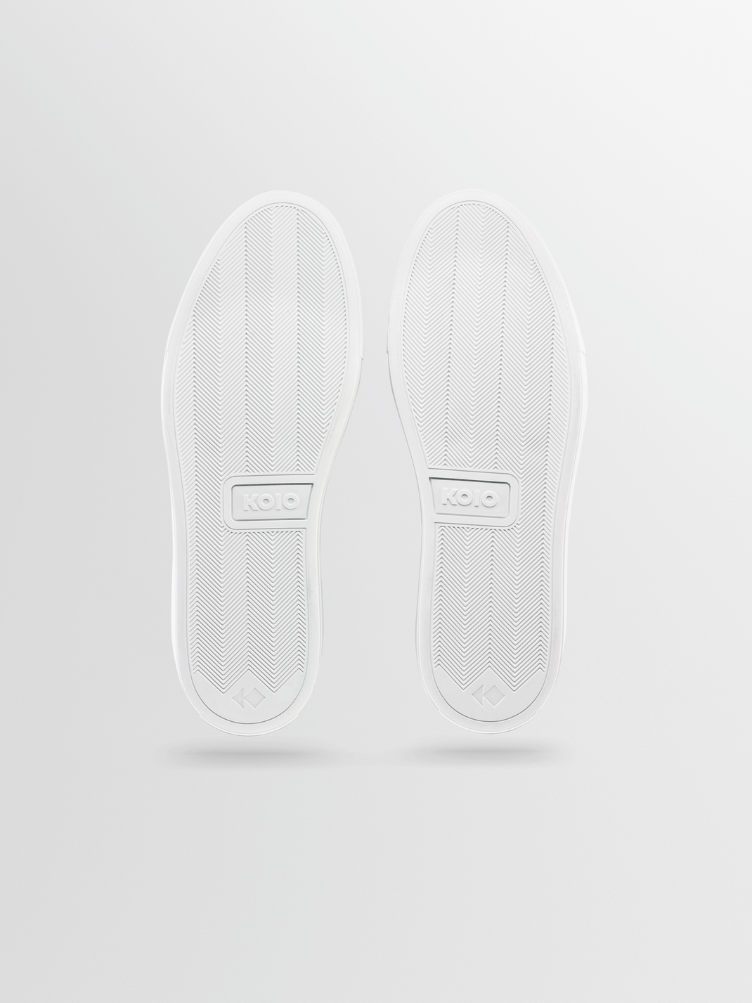 Bottom view of Portofino leather sneakers in triple white, showcasing chevron-patterned outsoles with KOIO branding