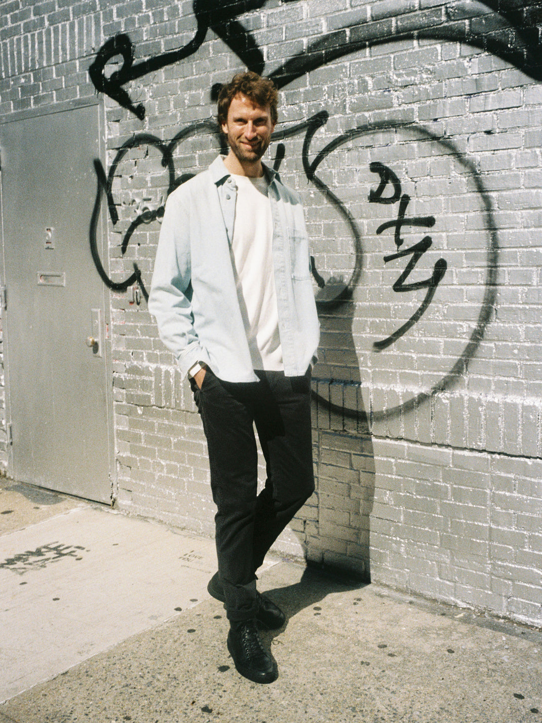 Man wearing black Primo high-top leather sneakers beside a graffiti-covered brick wall