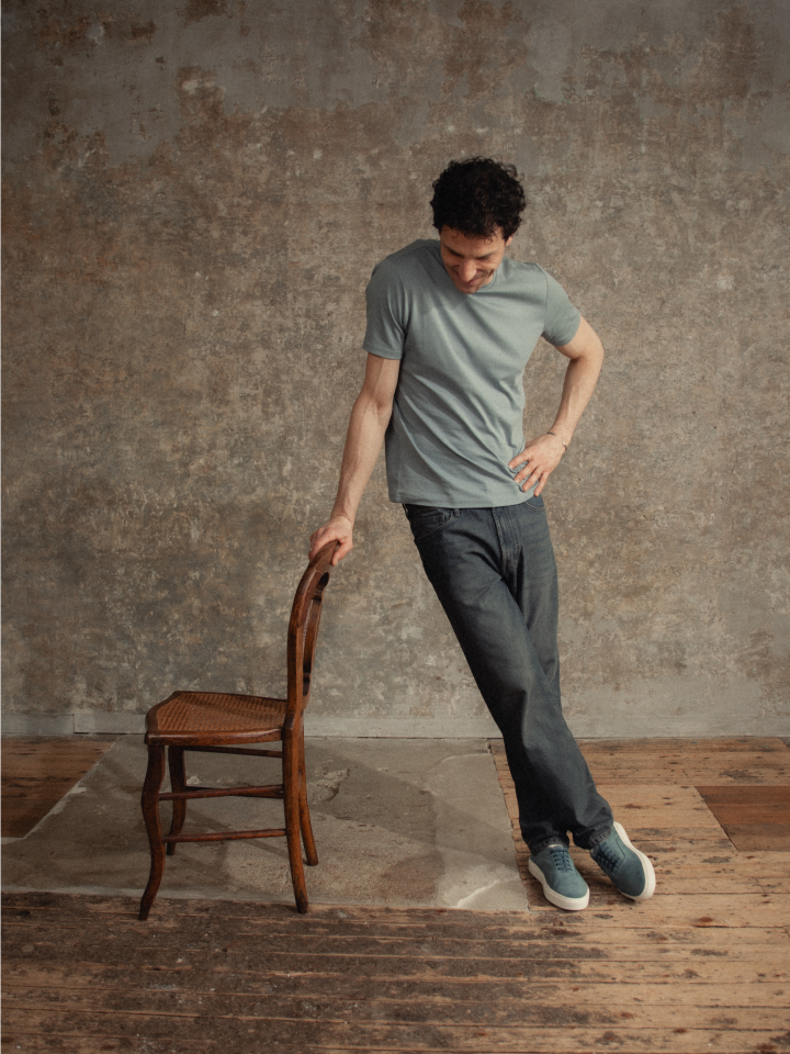 Man standing in gray shirt with jeans and blue Italian suede leather sneakers with laces and white rubber soles