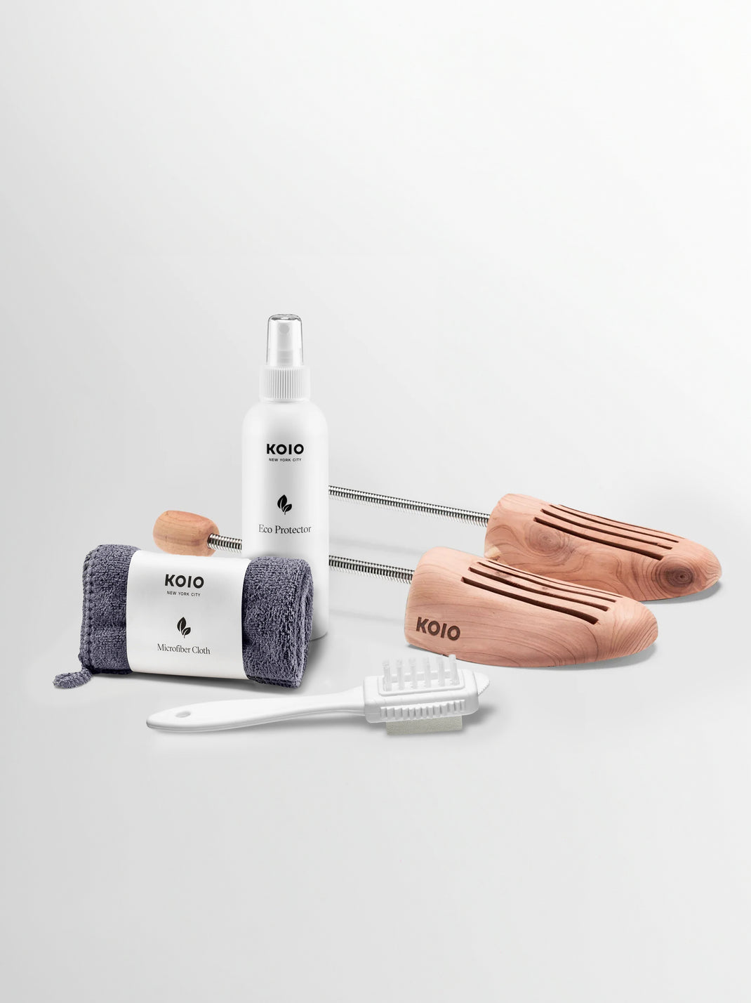 KOIO suede and nubuck care kit with Eco Protector, microfiber cloth, brush, and wooden shoe trees on white background