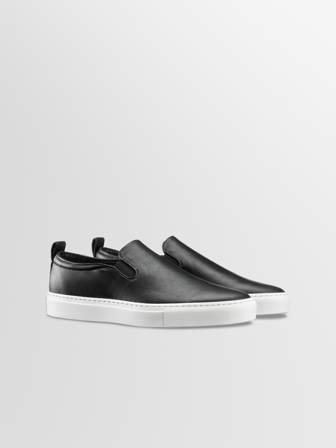 Three quarter view of Garda in Onyx slip on leather sneakers showcasing black leather uppers and white rubber soles