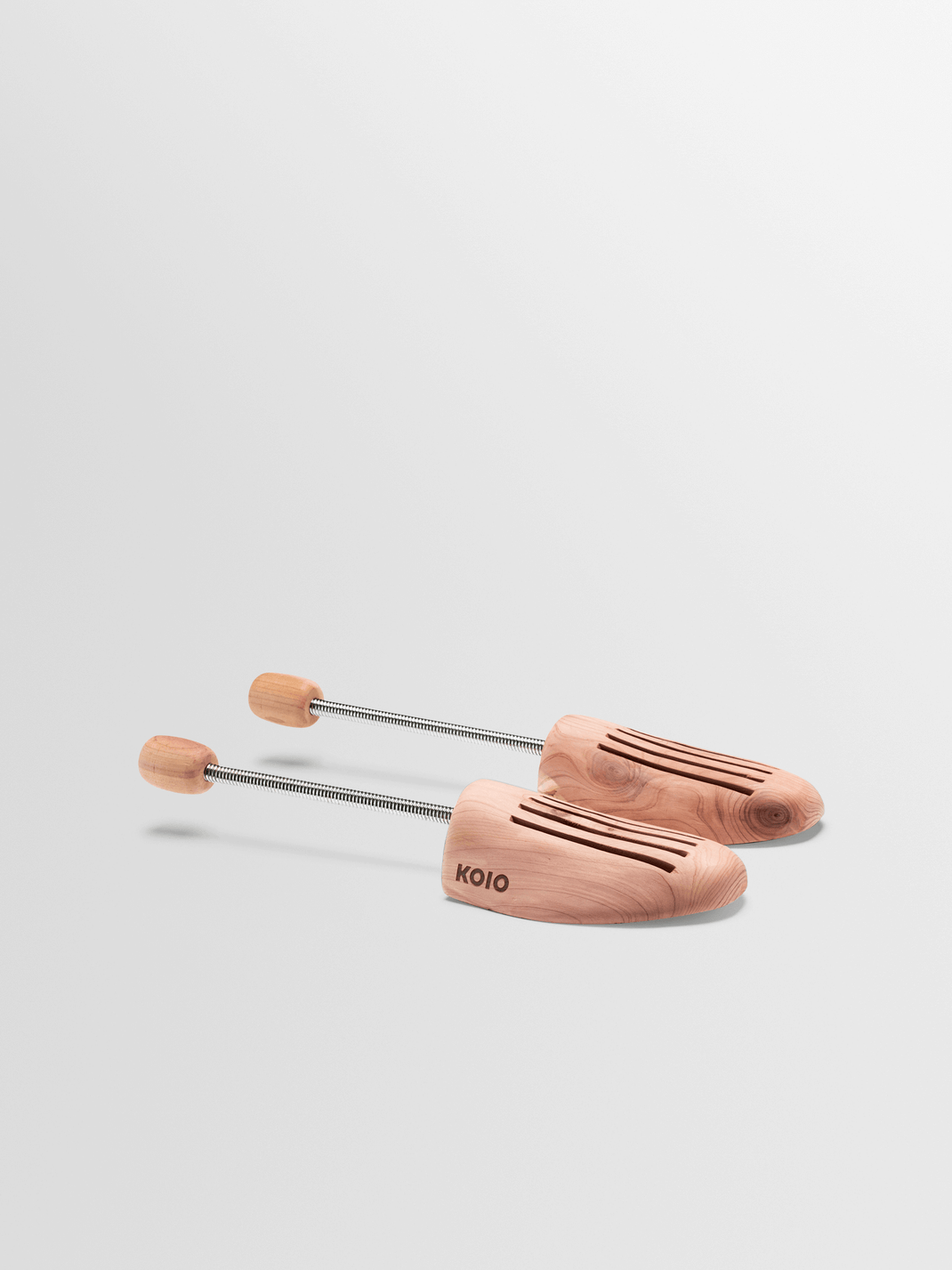 Three-quarter view of a pair of wooden shoe trees showcasing slotted wood forms and metal tension rods