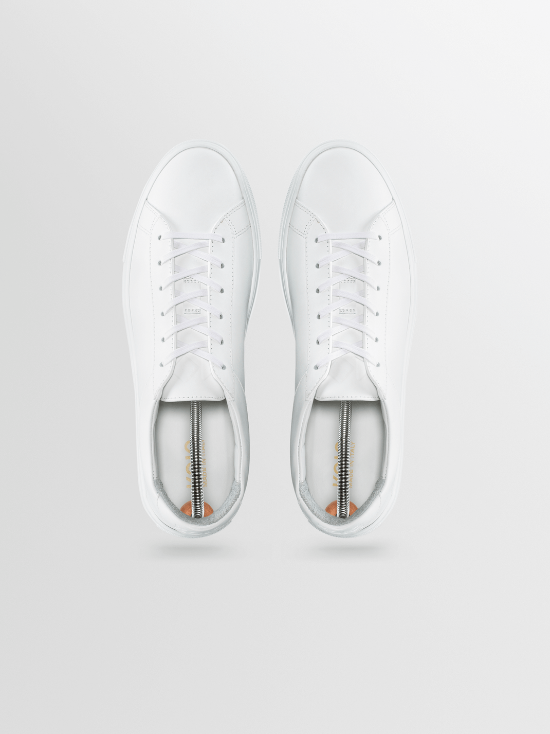 Top view of white sneakers showcasing metal shoe trees inside with a light gray background