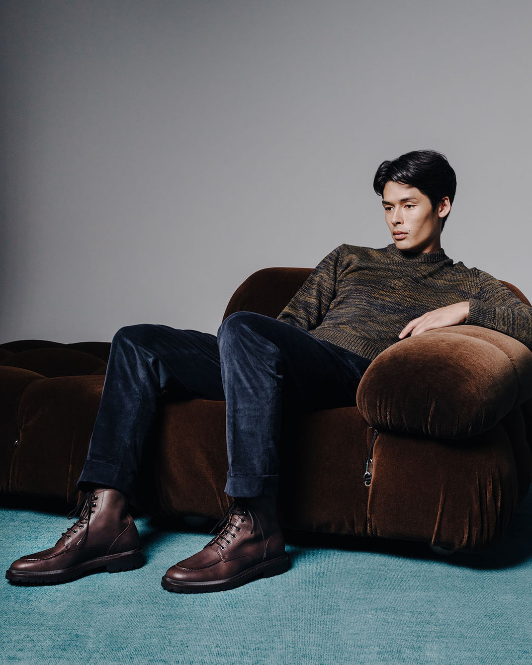 Front three-quarter view of Milo leather boots in chocolate showcasing lace-up design and rubber sole with a seated model