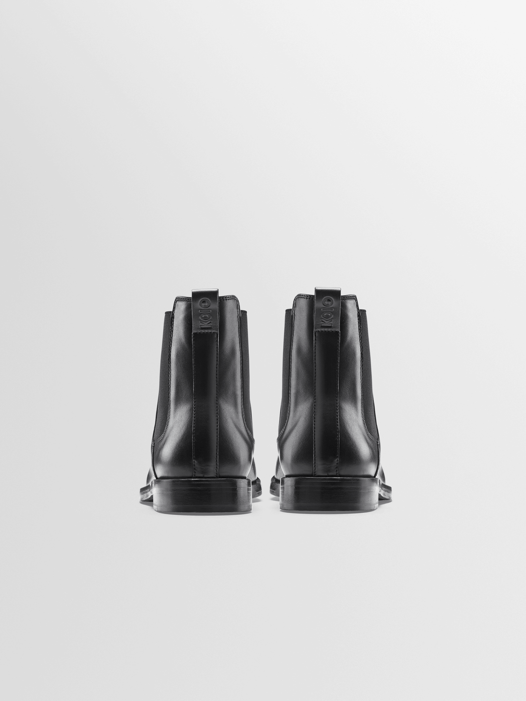 Rear view of Trento black leather Chelsea boots showcasing pull tabs and elastic side panels with a light gray background